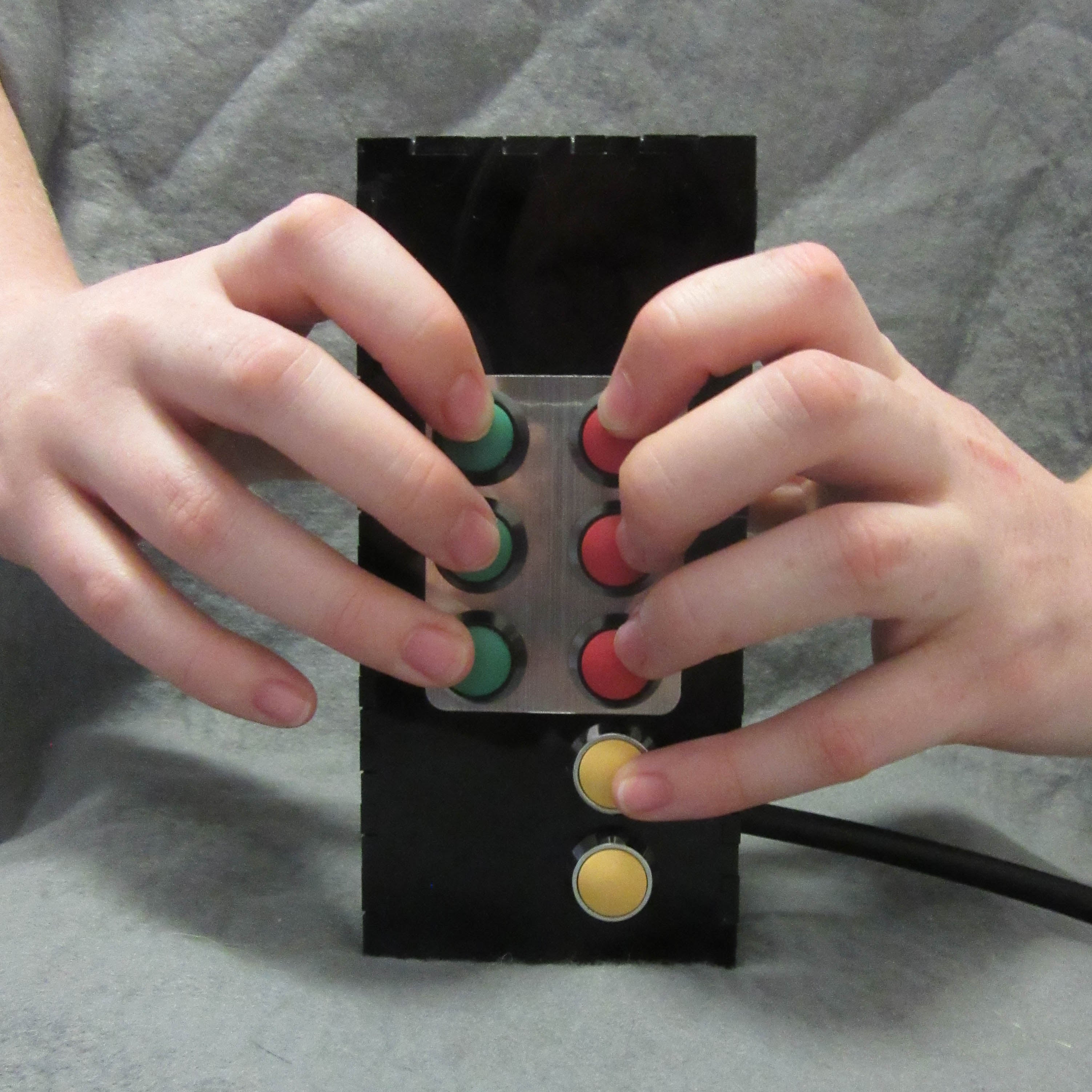 A black box with three red and three green buttons arranged as a braille cell. Two yellow buttons below.