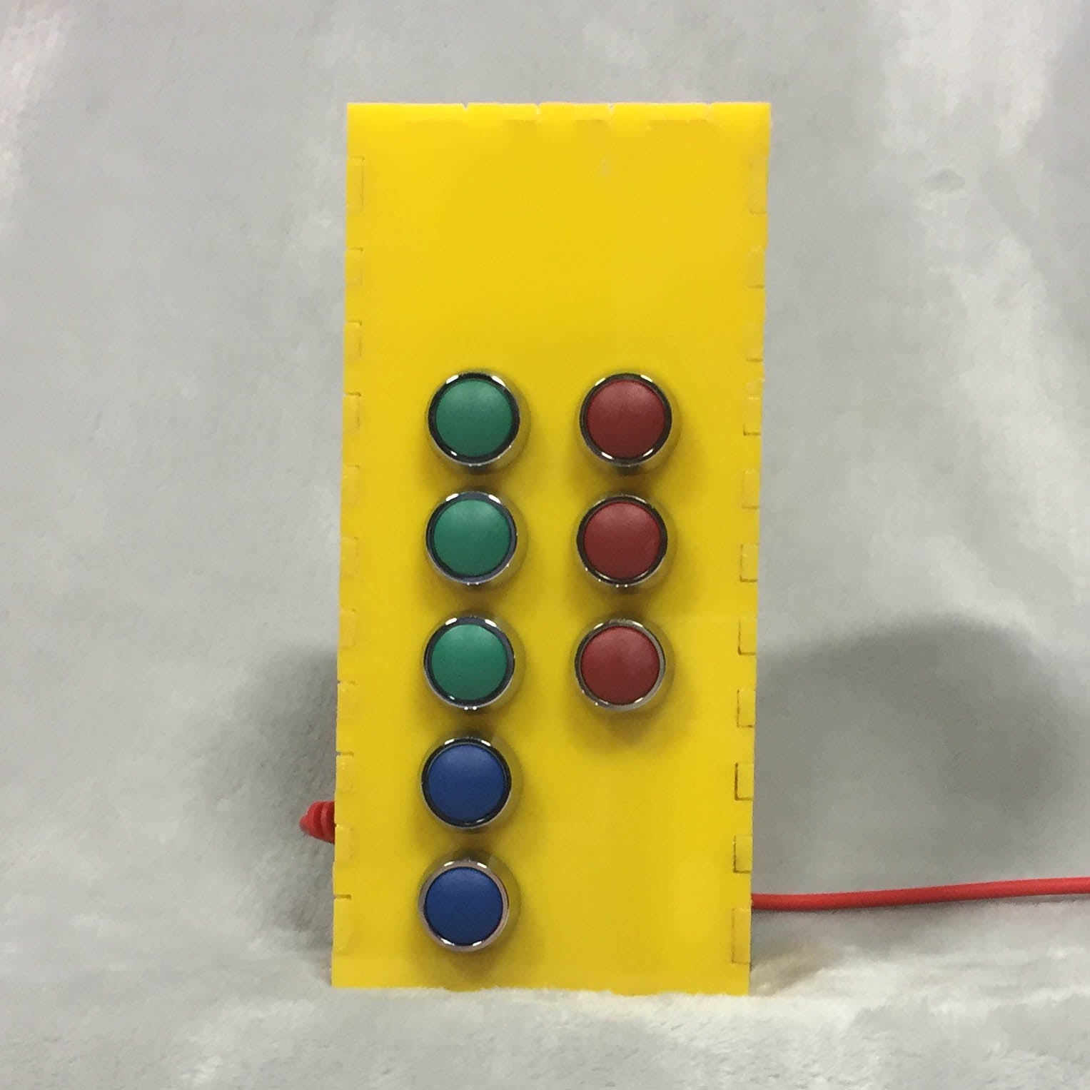 A yellow box with three red and three green buttons arranged as a braille cell. Two blue buttons below. 