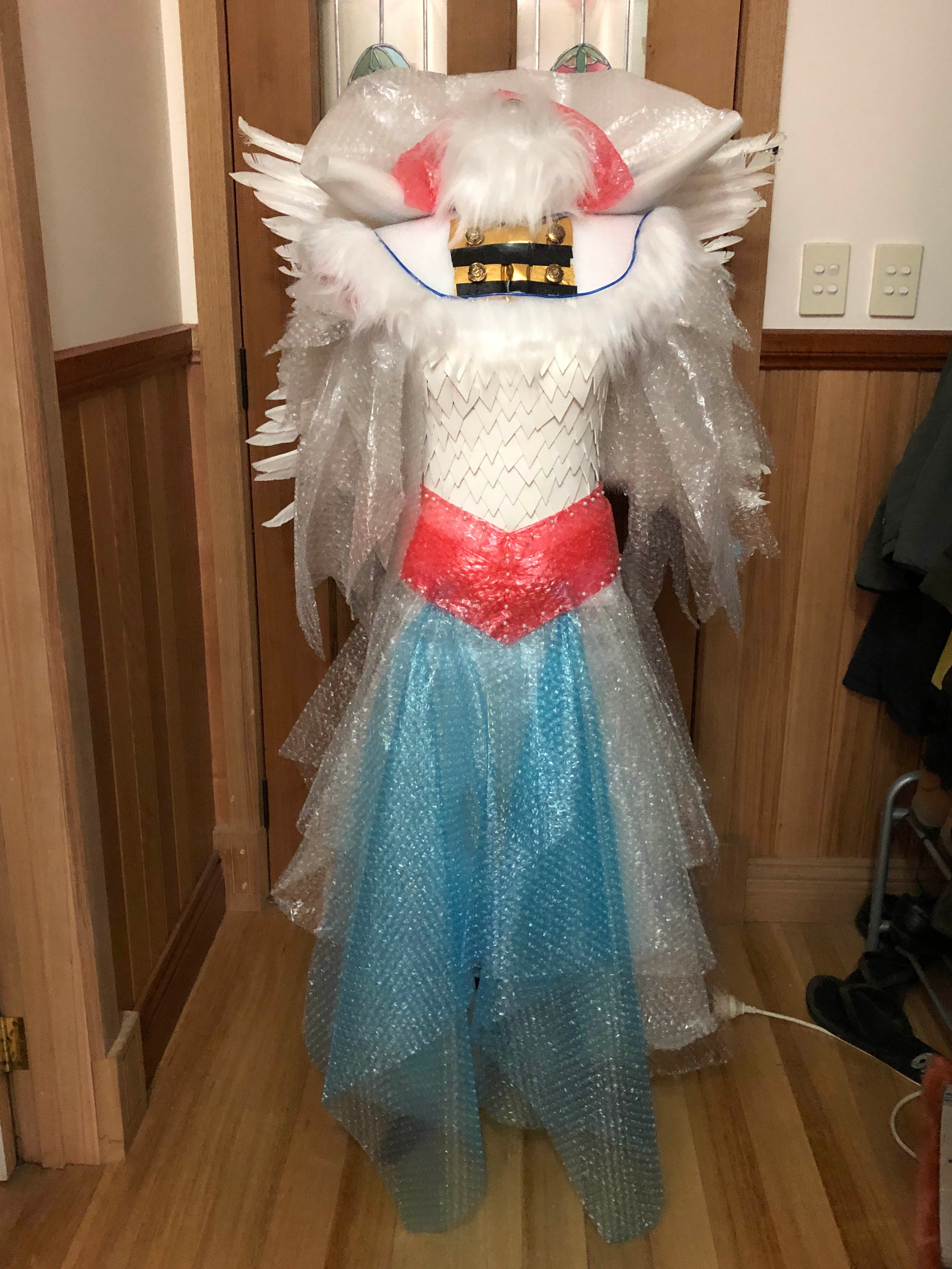 A model in a white dress that is made of bubble wrap with a foam tile bodice. There is a red belt and blue front decorative section.