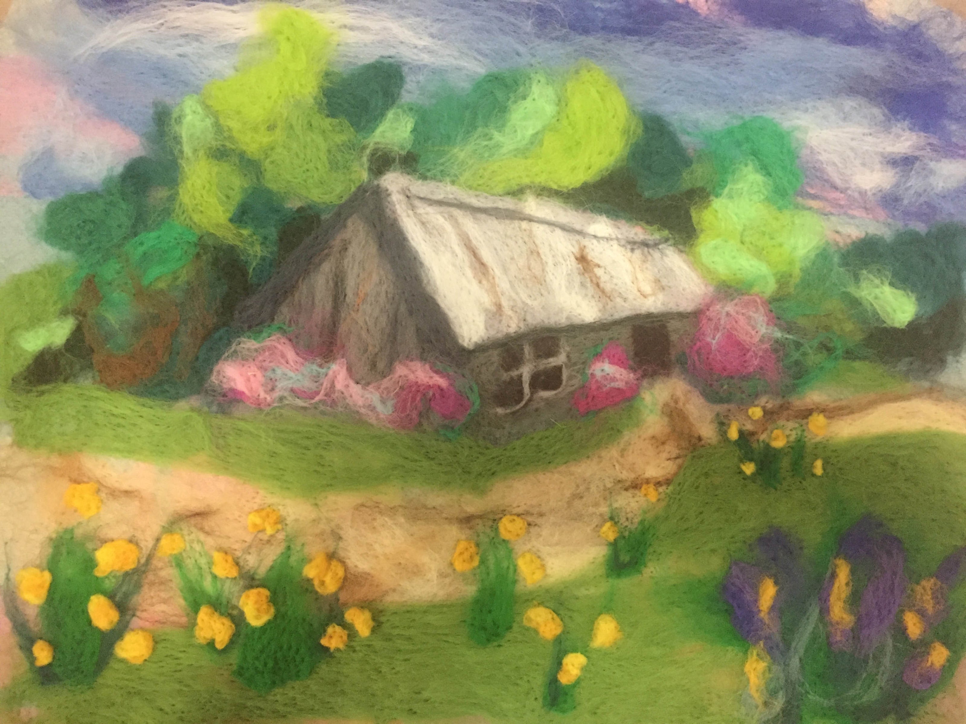 A dry felted picture of a house in amongst green trees with daffodils and flowers at the front. 