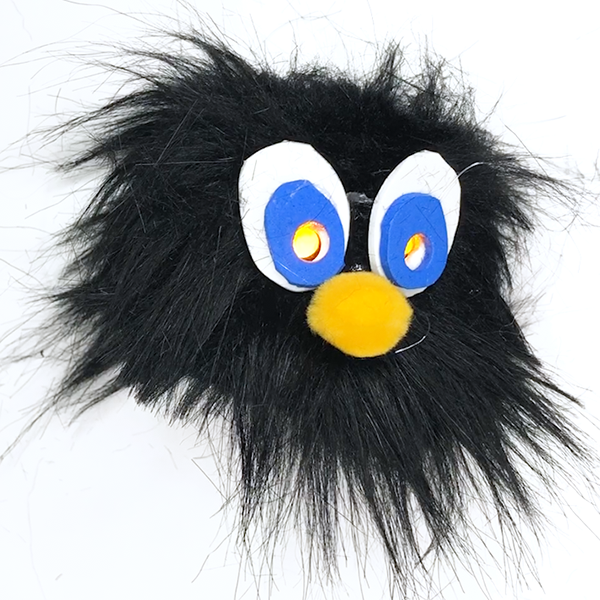 A Black fur character with white and blue felt around the yellow light up eyes and a yellow pom pom nose