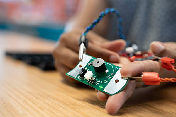 A green pub with a black buzzer. It is connected to 2 alligator clips that have twisted cables.