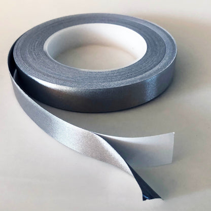 A Role of conductive tape which is open. There is an inch at the end showing the silver conductive tape separated from the white backing.