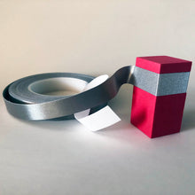 Load image into Gallery viewer, A roll of conductive tape with the end flexed around and attached to a red foam block. the white backing is still attached
