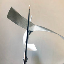 Load image into Gallery viewer, The silver tape being cut with scissors while the white tape hangs down
