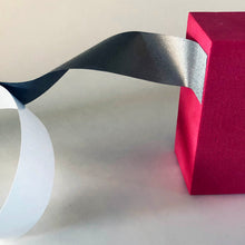 Load image into Gallery viewer, A flexible section of conductive tape is attached to a red block while it is still attached to the white backing
